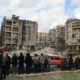 Menschen stehen vor zerstörten Häusern in Aleppo